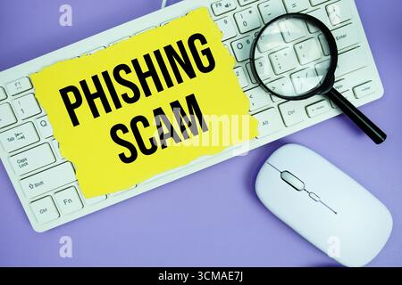 Papier jaune déchiré avec le texte "phishing Scam" placé sur un clavier blanc, une loupe et une souris d'ordinateur Banque D'Images