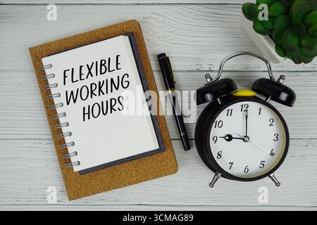 Horaires de travail flexibles texte écrit sur bloc-notes avec réveil sur fond en bois Banque D'Images