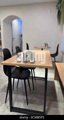 Intérieur de café moderne avec tables en bois et chaises noires, design minimaliste et atmosphère chaleureuse. Photo mobile Banque D'Images