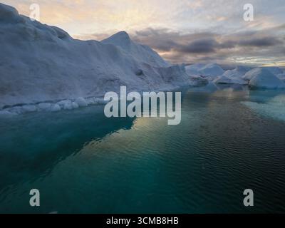 Eau turquoise calme entourée d'icebergs sous le ciel coloré du soir, baie de Disko, Groenland Banque D'Images