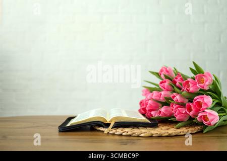 Bible ouverte avec des fleurs de tulipe sur bois clair Banque D'Images