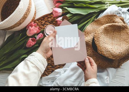 Mains de femme tenant une lettre dans une enveloppe artisanale. Fond rose, concept de fête des mères. Place pour votre texte. Banque D'Images