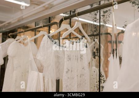 Robes de mariée de différents styles accrochés sur des supports dans une boutique chic, mettant en valeur des tissus délicats et des motifs complexes. Banque D'Images