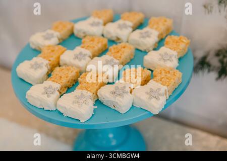 Des friandises croustillantes de riz colorées recouvertes de glaçage blanc se tiennent sur un stand de gâteaux lumineux lors d'une réunion hivernale amusante. Banque D'Images