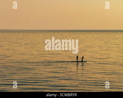 Samothraki, Grèce – activité de SUP à Kipos Beach pendant le coucher du soleil, avec deux personnes silhouettées sur une planche à paddleboard au-dessus des eaux calmes, des reflets dorés, et Banque D'Images