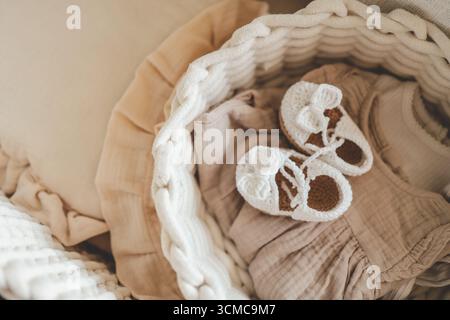 Chaussons tricotés et choses pour un nouveau-né dans le berceau. Banque D'Images