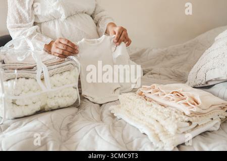La femme enceinte se prépare pour la maternité, emballant des trucs pour bébé. femme enceinte préparant et planifiant des vêtements pour bébé. Banque D'Images