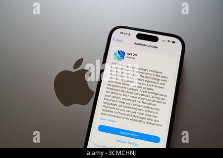 Mise à jour iOS 26 sur iPhone à côté du logo Apple sur MacBook en mode lumière. Stafford, Royaume-Uni, 15 septembre 2025 Banque D'Images