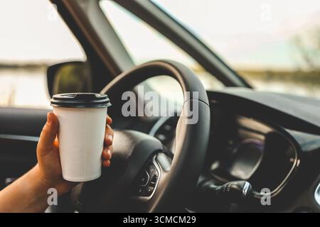 Tasse de papier avec café à la main, voyageant en voiture. Banque D'Images