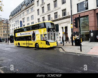 Manchester, Royaume-Uni - 14 septembre 2025 : bus à impériale Bee Network, rue de Manchester avec piétons et bâtiments visibles. Banque D'Images