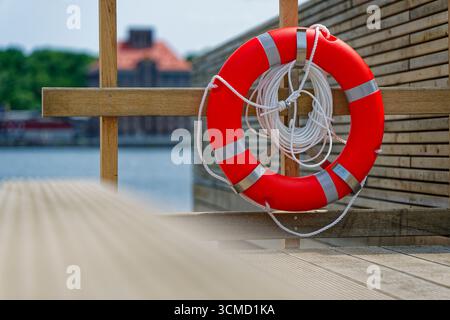 Des planches de jetée en bois bordent l'eau, un rail bas longe le côté et une bouée de sauvetage lumineuse avec un cordon blanc est suspendue prête. La petite vue sur le port se sent qu Banque D'Images