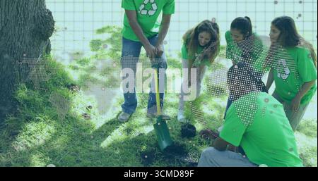 Bénévoles portant des chemises vertes plantant des jeunes arbres dans le parc, avec excavatrice de trou de poteau et bouteille d'eau Banque D'Images