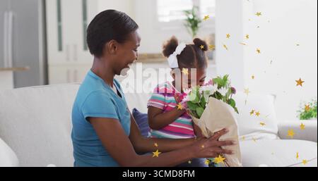 Mère et fille sentant des fleurs roses et blanches enveloppées de papier sur un canapé gris clair dans le salon Banque D'Images