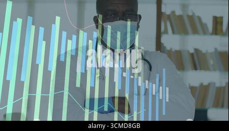 Docteur noir debout croisant les bras dans le cabinet médical, portant un masque, avec stéthoscope, tableaux de données Banque D'Images