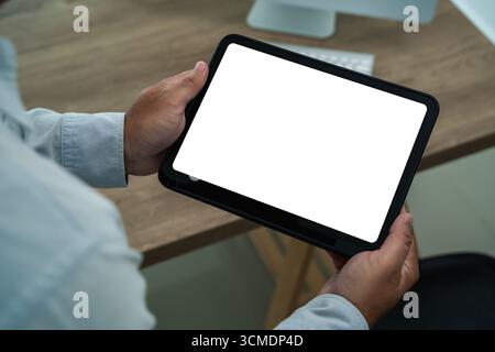 Personne tenant une tablette numérique avec écran blanc dans un bureau moderne, idéal pour présenter la conception d'interface utilisateur, prototype d'application mobile, signature électronique et affaires cont Banque D'Images