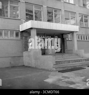 Cette photographie d'archives de 1987 offre une vue rapprochée de l'entrée principale de la nouvelle école n° 17 à Sloviansk, RSS d'Ukraine. Le design fonctionnaliste de l'entrée, avec son auvent en béton, ses portes vitrées et ses plaques officielles, est caractéristique des bâtiments publics de l'époque perestroïka. En tant que porte d'entrée vers l'éducation pour un nouveau microdistrict résidentiel, cette entrée de l'école est un symbole puissant et nostalgique de l'enfance, du système éducatif soviétique et de la vie quotidienne de la communauté dans les dernières années de l'URSS Banque D'Images