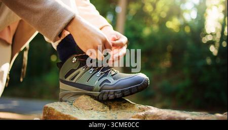 Personne, mains et chaussures attachantes sur la roche pour la préparation de la randonnée, sentier ou chemin dans la forêt extérieure. Gros plan, randonneur ou préparation avec cravate, lacets ou Banque D'Images