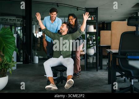 Équipe multiraciale heureuse, les gens d'affaires ayant du plaisir à monter sur des chaises dans la salle de bureau Banque D'Images