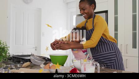 Guider la mère et la fille portant des tabliers craquant l'oeuf sur l'îlot de cuisine, avec bol à mélanger vert Banque D'Images