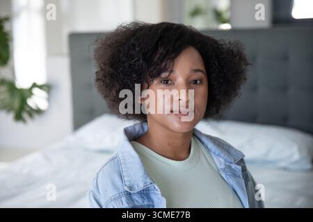 Femme afro-américaine debout dans la chambre par lit touffeté et plante en pot par des rideaux transparents Banque D'Images