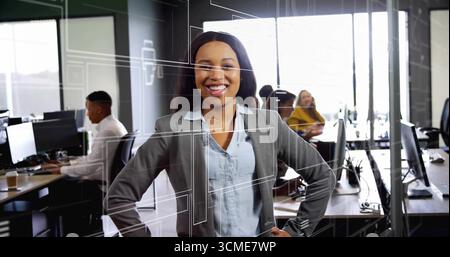 Femme cadre souriante portant un blazer gris debout dans un bureau d'entreprise, avec des bureaux et des ordinateurs Banque D'Images