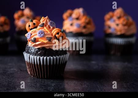 Cupcakes d'Halloween avec décoration de citrouille saupoudrée sur table en bois rustique et fond violet Banque D'Images