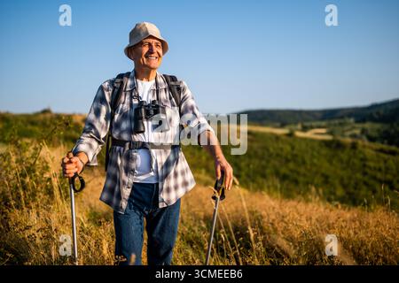 Portrait de randonneur senior heureux avec sac à dos et bâton de randonnée profitant de la randonnée dans la nature. Banque D'Images