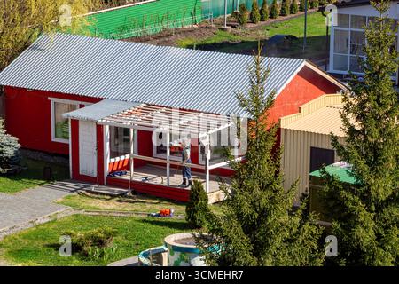 Russie -17 mai 2024. Homme travaillant sur une nouvelle véranda attachée à la maison rouge, créant un espace extérieur confortable pour la détente en famille, barbecues et soirée d'été Banque D'Images