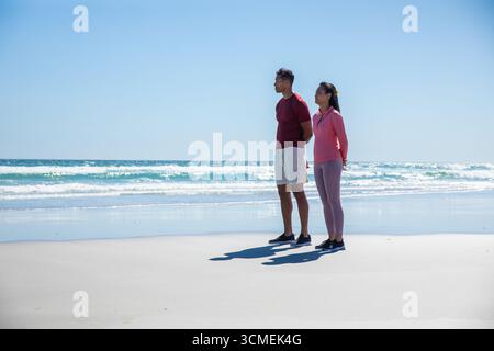 Couple diversifié debout sur la plage face à l'océan dans des chaussures athlétiques noires, espace de copie Banque D'Images