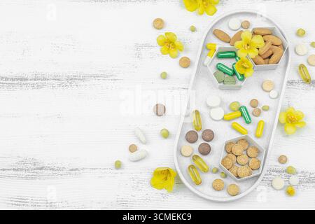 Compléments alimentaires assortis, vitamines et capsules de phytothérapie avec fleurs de molène fraîche (Verbascum) sur un fond de bois blanc, soins de santé a Banque D'Images