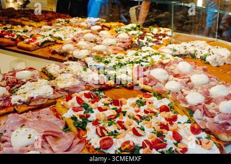 assortiment de pizzas italiennes al taglio avec mozzarella, mortadelle, crevettes, tomates et autres garnitures fraîches présentées derrière un comptoir en verre dans une pizza s. Banque D'Images