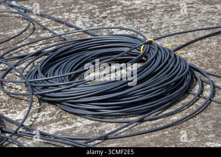 Gros plan d'une bobine de fils électriques noirs, ou de câbles, sur un sol en béton gris, mettant en évidence les thèmes industriels, de la construction et de l'alimentation. Banque D'Images