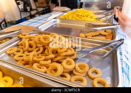 Plateaux de rondelles d'oignon frites croustillantes, de nuggets de poulet et de frites prêtes à servir dans un comptoir de cuisine de rue libre-service. Banque D'Images