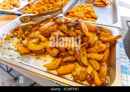 Plateaux de rondelles d'oignon frites croustillantes, de nuggets de poulet et de frites prêtes à servir dans un comptoir de cuisine de rue libre-service. Banque D'Images