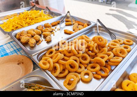 Plateaux de rondelles d'oignon frites croustillantes, de nuggets de poulet et de frites prêtes à servir dans un comptoir de cuisine de rue libre-service. Banque D'Images