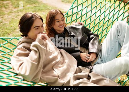 Un jeune couple se détend dans un hamac, partageant rire et chaleur dans un cadre de parc ensoleillé. Banque D'Images