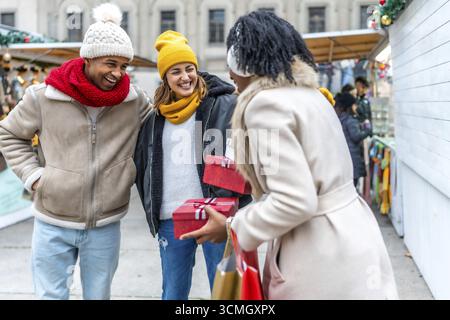 Heureux amis échangeant des cadeaux de noël tout en profitant d'une promenade dans un marché hivernal festif Banque D'Images