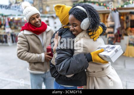 Heureux amis échangeant des cadeaux de noël et serrant dans un marché de noël pendant les vacances d'hiver Banque D'Images
