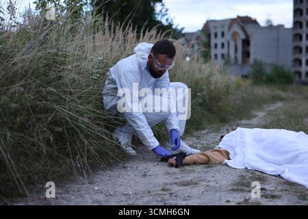 Expert médico-légal travaillant sur la scène de crime avec un cadavre dehors Banque D'Images