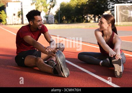 Couple souriant en vêtements de sport s'étirant avant de courir au stade Banque D'Images