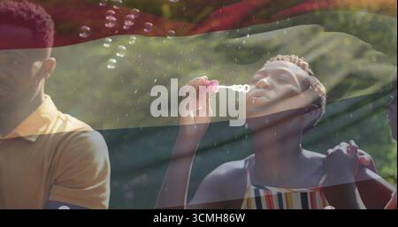 Femme soufflant dans la robe de soleil créant des bulles dans le jardin ensoleillé, avec la baguette de bulle rose superposition rayée Banque D'Images