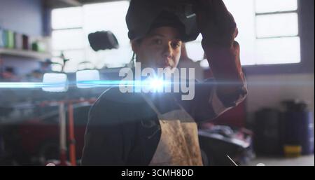 Visière de casque de levage femme soudeur portant tablier lourd et gants dans le garage, avec évasement d'arc de soudure Banque D'Images