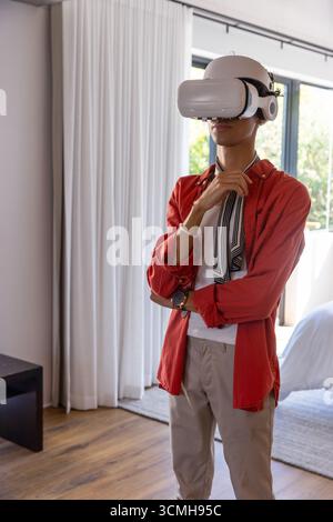 Homme debout près de la fenêtre portant un casque de réalité virtuelle et une écharpe rayée dans la chambre Banque D'Images