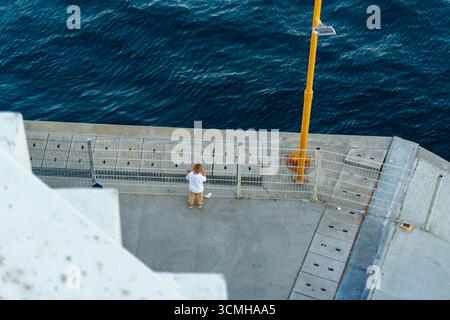 Une photo au-dessus du ciel d'un enfant debout seul sur une jetée en béton, regardant les eaux bleues profondes du Bosphore. La scène capture un moment calme Banque D'Images