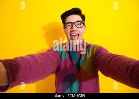 Jeune homme ludique dans un pull géométrique coloré sortant de sa langue sur un fond jaune vif Banque D'Images