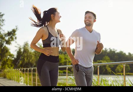 Couple sportif courant joyeusement le long du chemin extérieur, joyeux amis jogging le jour ensoleillé Banque D'Images
