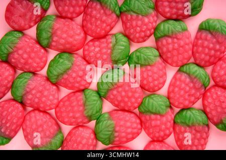 De nombreux bonbons en forme de fraise formant un motif coloré et appétissant sur un fond rose Banque D'Images