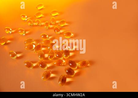 De nombreuses capsules d'huile de poisson sont dispersées sur une surface orange vibrante, offrant une source puissante d'acides gras oméga-3 pour des bienfaits pour la santé Banque D'Images