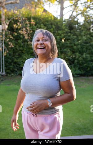 Femme afro-américaine senior debout, souriant dans la cour par le cadre de balançoire en métal portant le poignet Banque D'Images