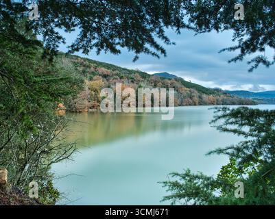 Lac d'automne brumeux encadré par la forêt - Une photo longue exposition d'un lac paisible et brumeux en automne, encadré par la forêt environnante avec son foli changeant Banque D'Images